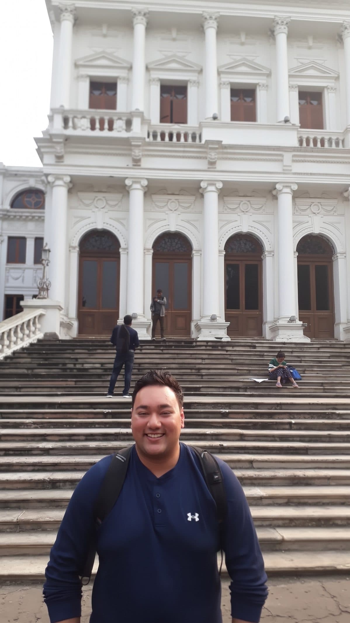 Areeb Uzzaman smiling on the front steps of the National Library of Kolkata, a white colonnaded building